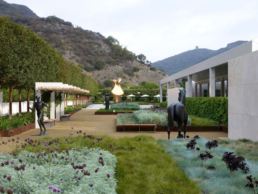 Sculpture garden with modern art pieces, greenery, and mountainous backdrop under an overcast sky.