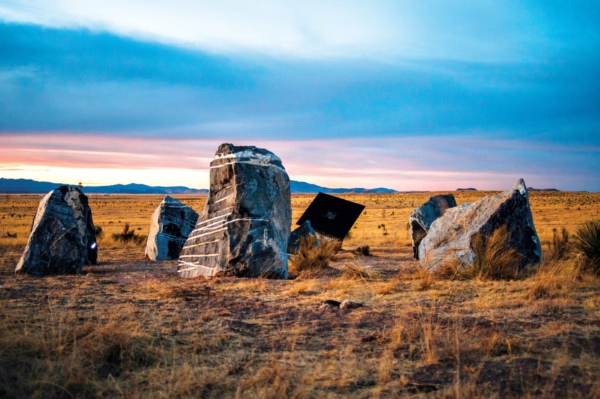 Large rocks arranged in a circle on a dry grass field under a dramatic sunset sky.