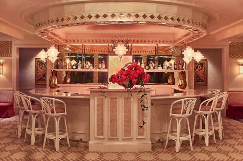 Luxurious hotel bar with elegant white chairs, ornate lighting, and vibrant floral arrangement on the counter.