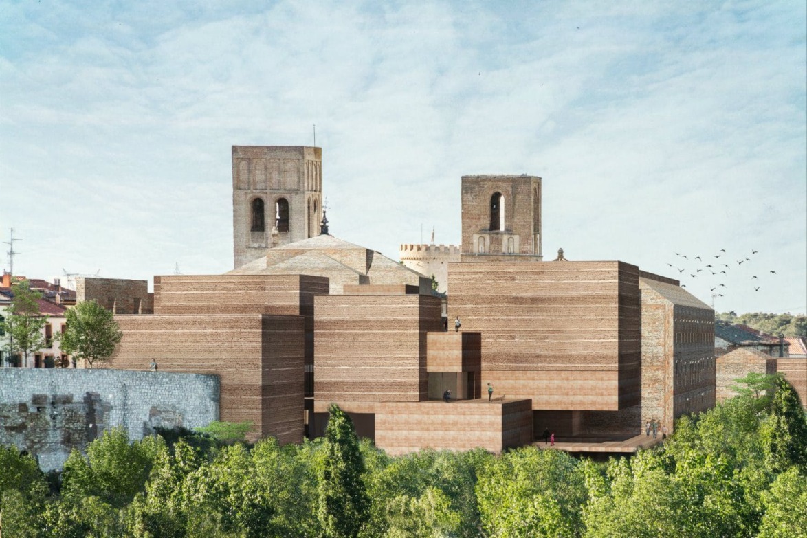 Modern architectural building with brown brick facade and towers surrounded by green trees under a blue sky.