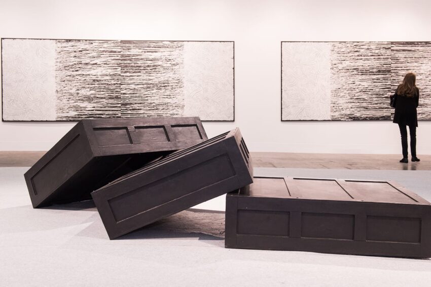 Modern art exhibit featuring large black sculptures and abstract black-and-white paintings with a person observing.