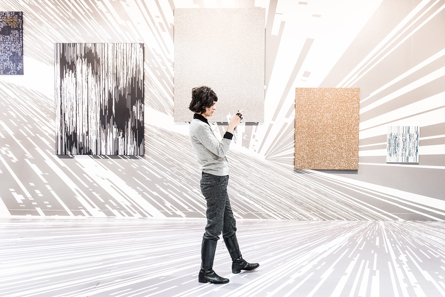 Person photographing abstract artwork in a modern gallery with patterned walls and floors.