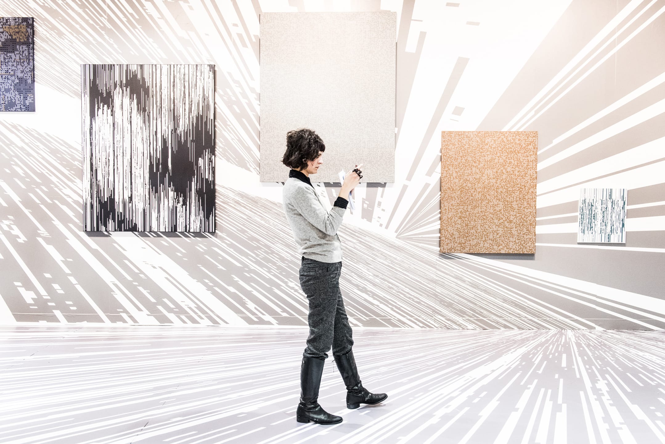 Person in a gallery taking a photo of abstract paintings on the wall, with a striking geometric floor design.