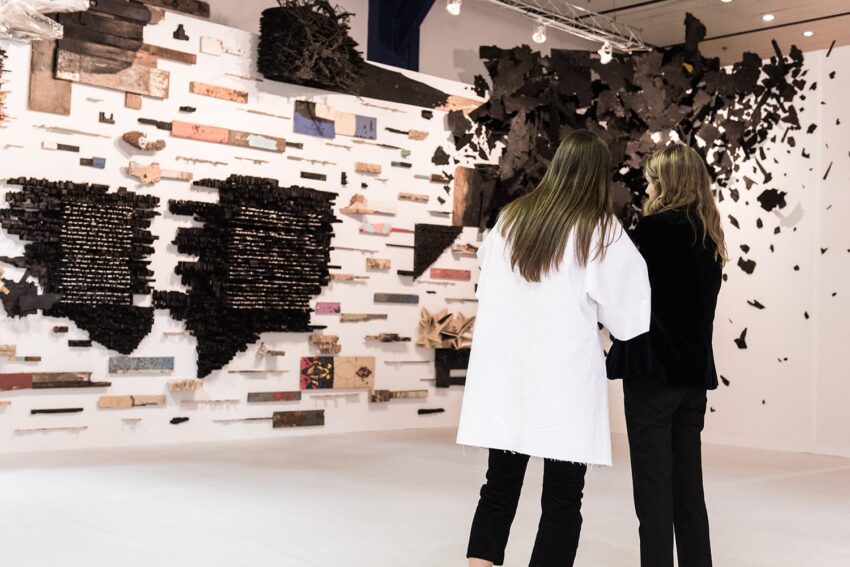 Two women viewing a modern art exhibit with abstract wall installations in a gallery space.