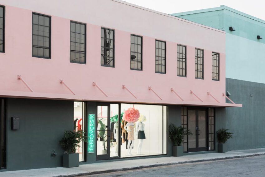 Exterior of a stylish store with a pink facade and large windows displaying mannequins and a floral decoration.
