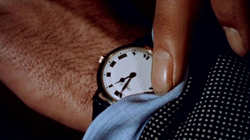 Close-up of a person's hand wearing a classic wristwatch with Roman numerals, partially covered by a blue and black polka-dot sleeve.