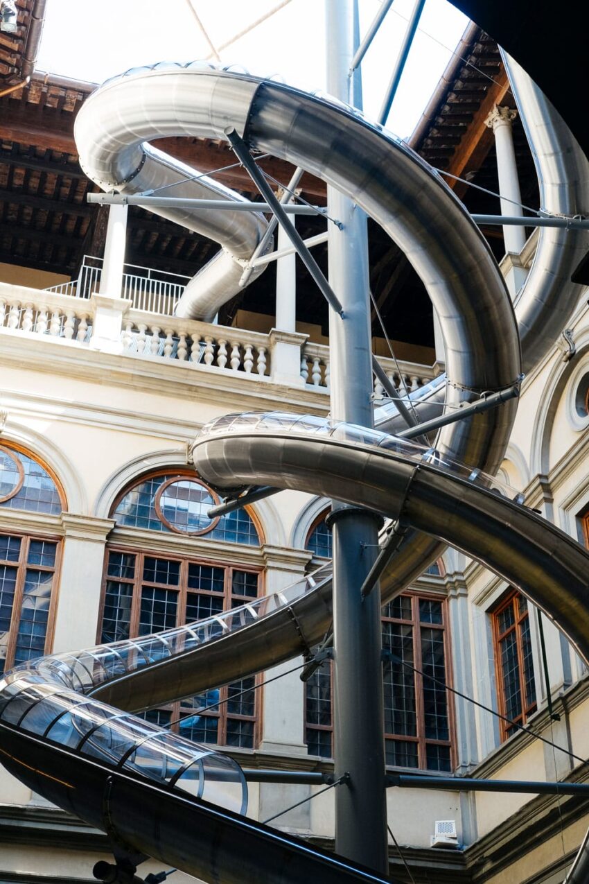 Curved metal slide spiraling down the side of a historic building with arched windows and ornate details.