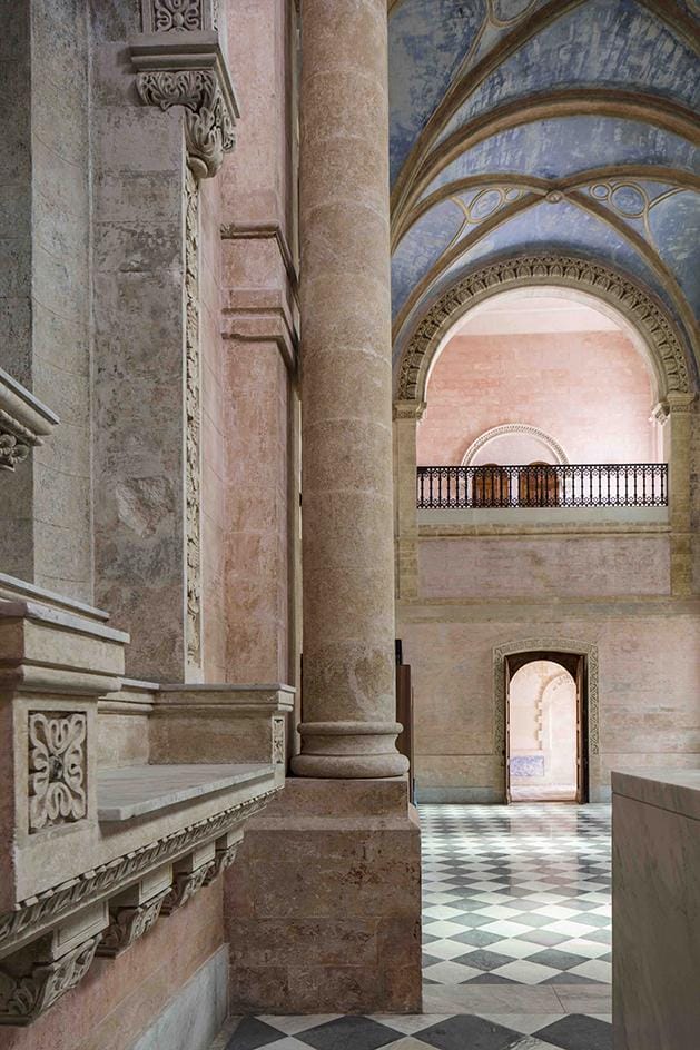 Elegant interior of a historic building with stone columns, vaulted ceilings, and checkered floor tiles.