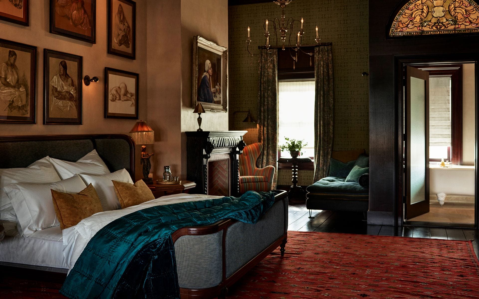 Cozy bedroom with artwork on walls, plush bed, vibrant rug, and adjacent sitting area with a window view.