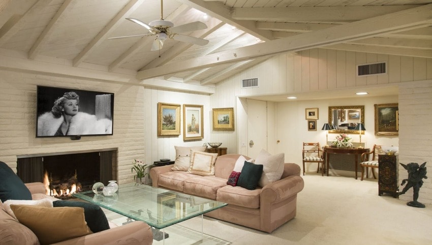 Living room with high ceilings, fireplace, sofa, glass coffee table, and framed portrait on TV above the mantle.