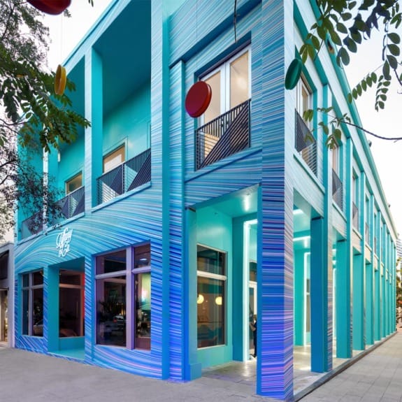 Colorful turquoise and blue striped building facade with large windows and unique architecture, trees in foreground