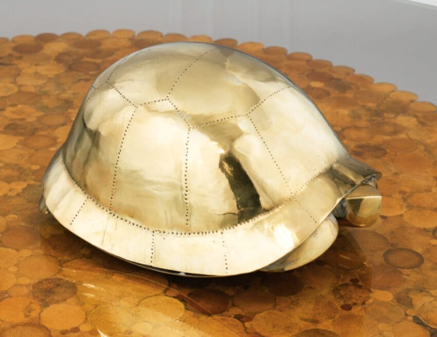 A shiny gold turtle shell sculpture displayed on a textured brown surface.