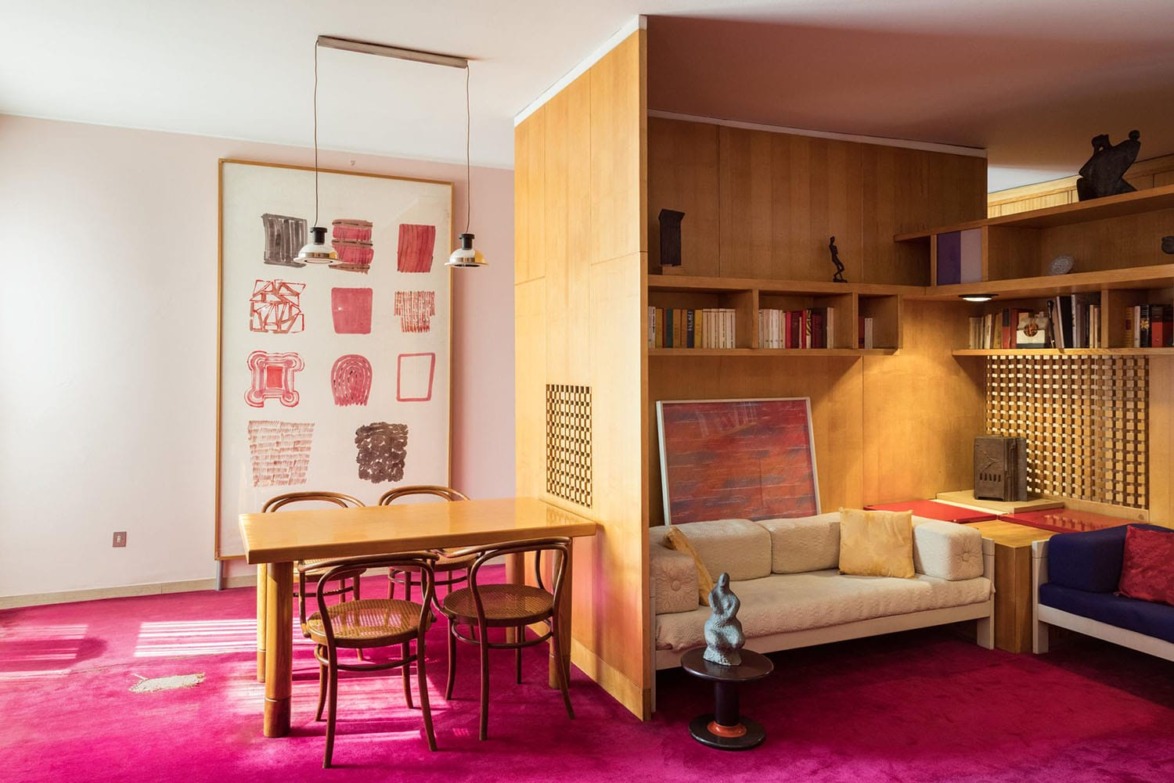 Mid-century modern living room with wooden furniture, abstract art, pink carpet, and cozy seating area.