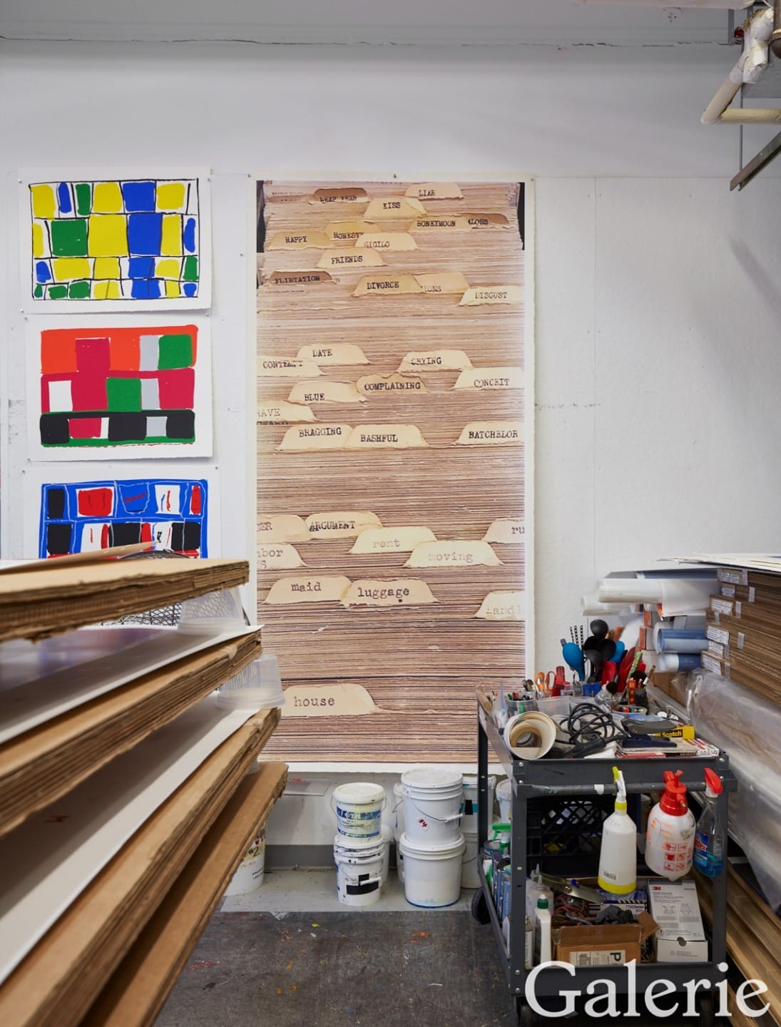 Art studio with colorful abstract paintings, wooden panels, and shelves filled with art supplies and tools.
