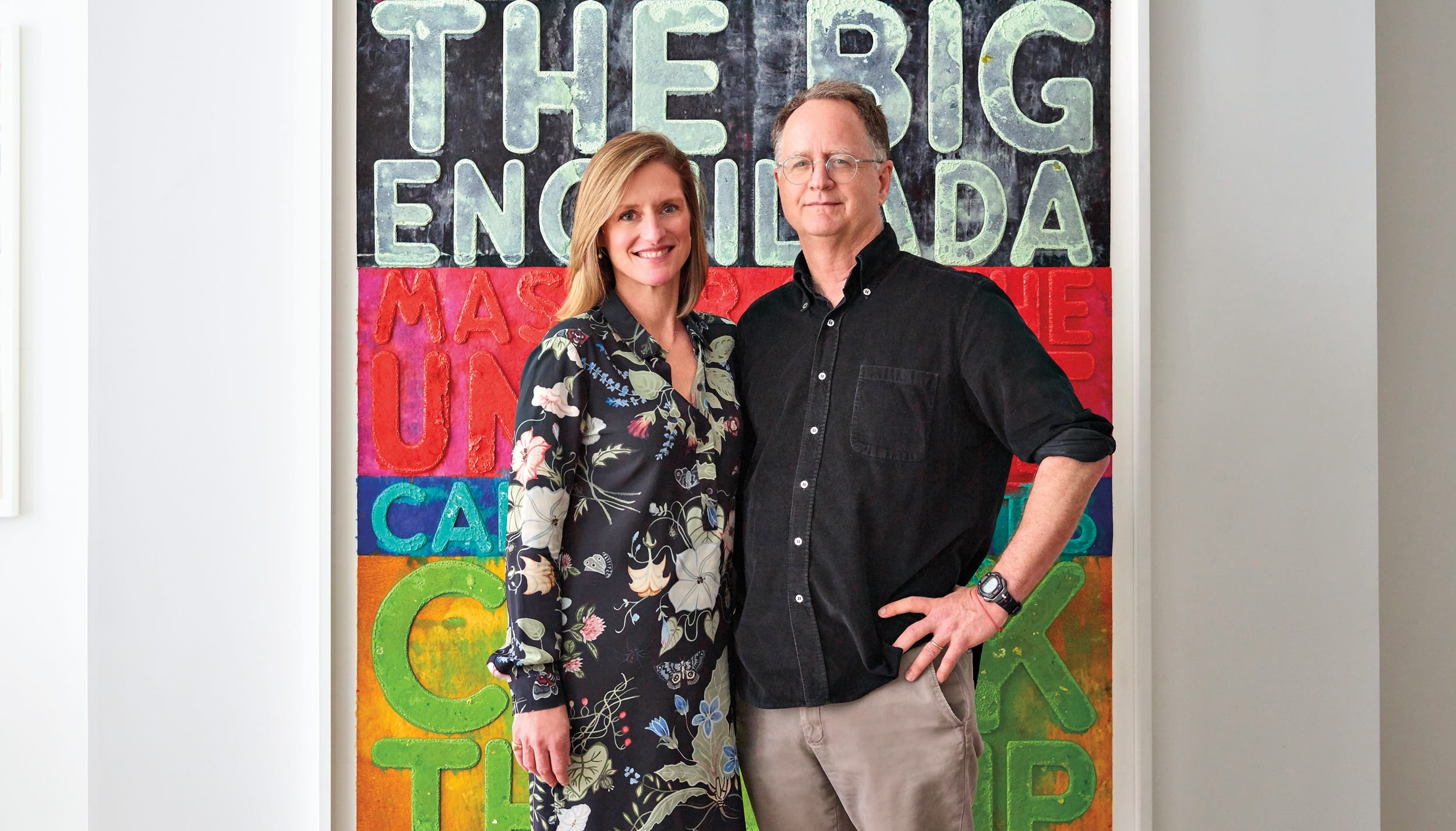 Two people standing and smiling in front of a colorful poster with text.