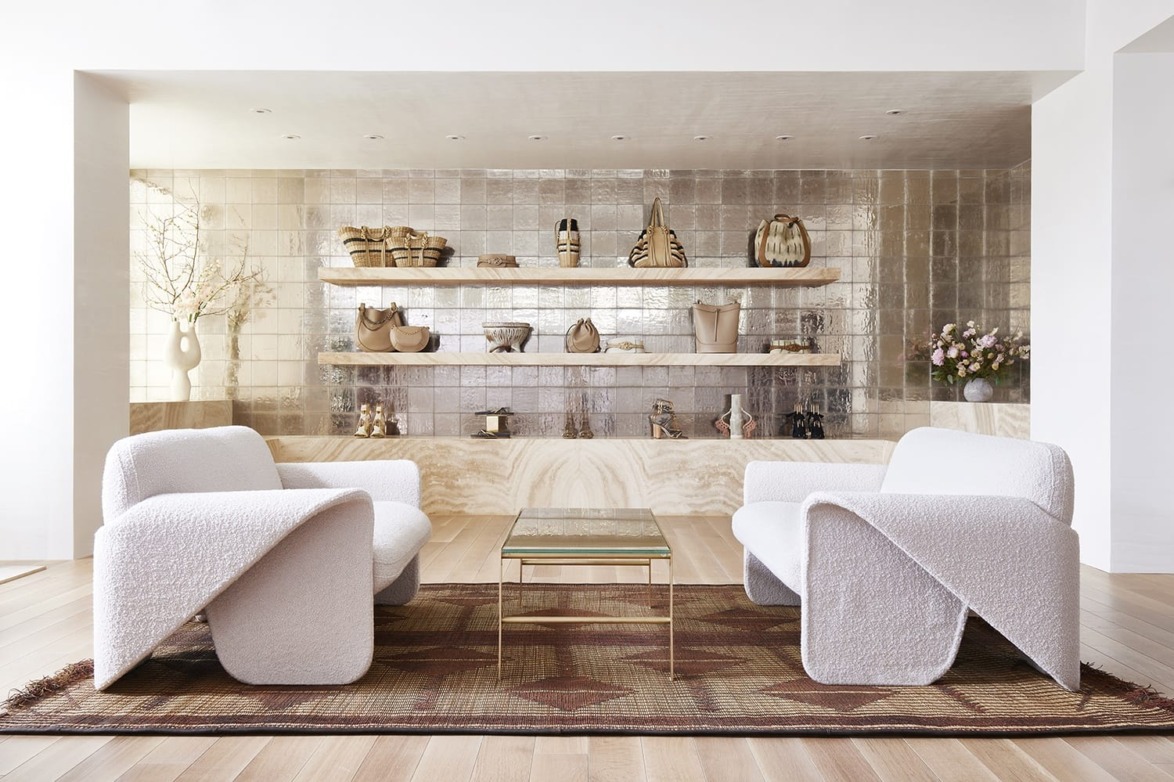 Modern living room with two white armchairs, a glass coffee table, and decorative shelves against a tiled wall.
