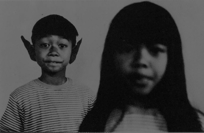 Two children, one with large pointed ears, stand side by side in a black and white photo, both wearing striped shirts.