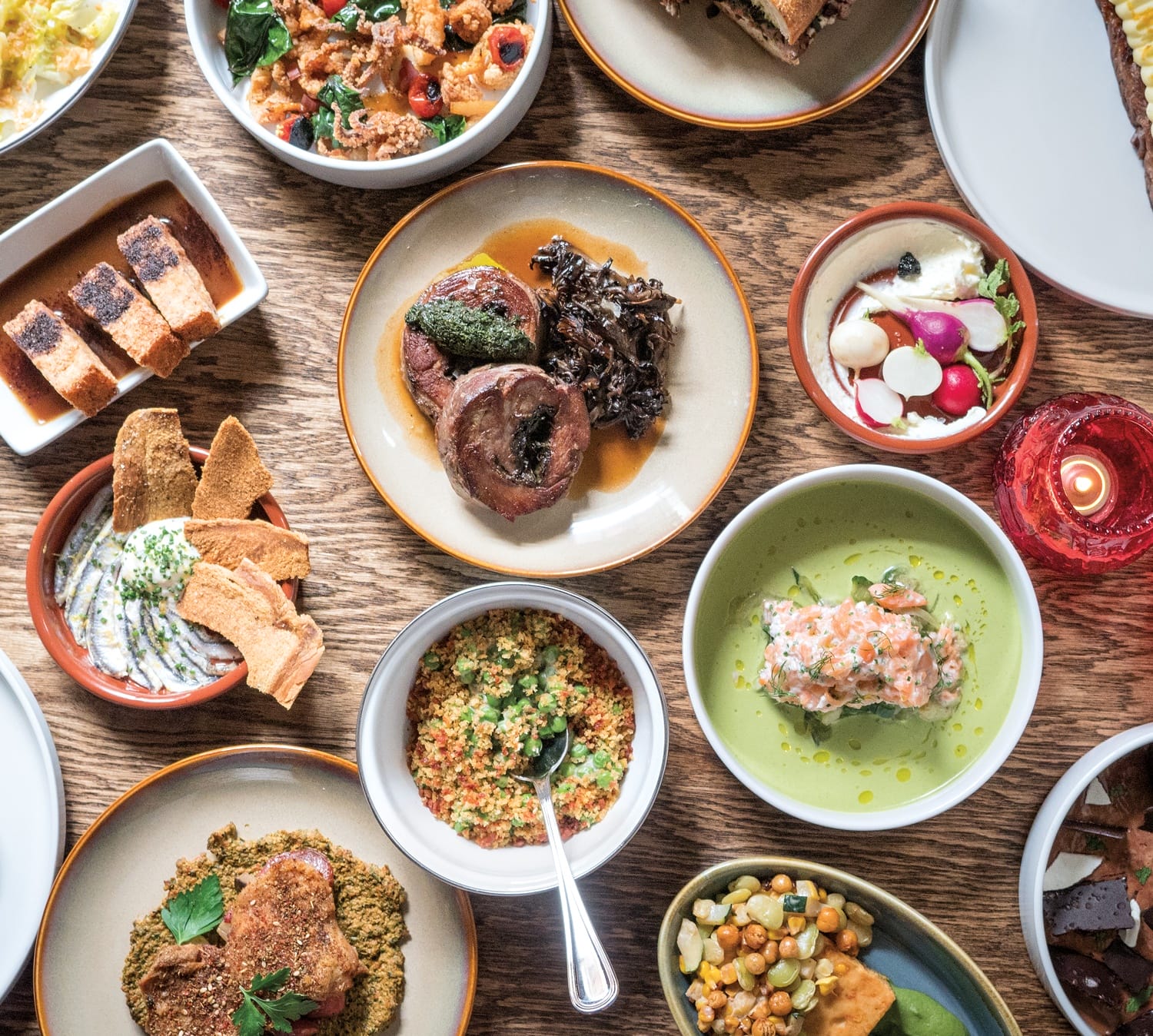 Assorted dishes including meats, salads, and vegetables on a wooden table, showcasing a variety of vibrant, colorful meals.