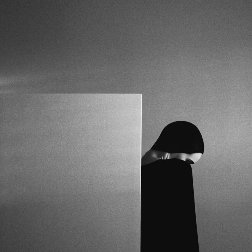Abstract black and white image of a person partially hidden behind a wall, creating a mysterious and minimalist scene.