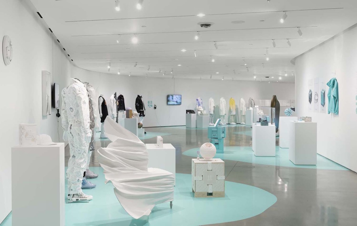 Modern art exhibit with abstract sculptures and fashion displays in a well-lit gallery space with white walls and turquoise accents.