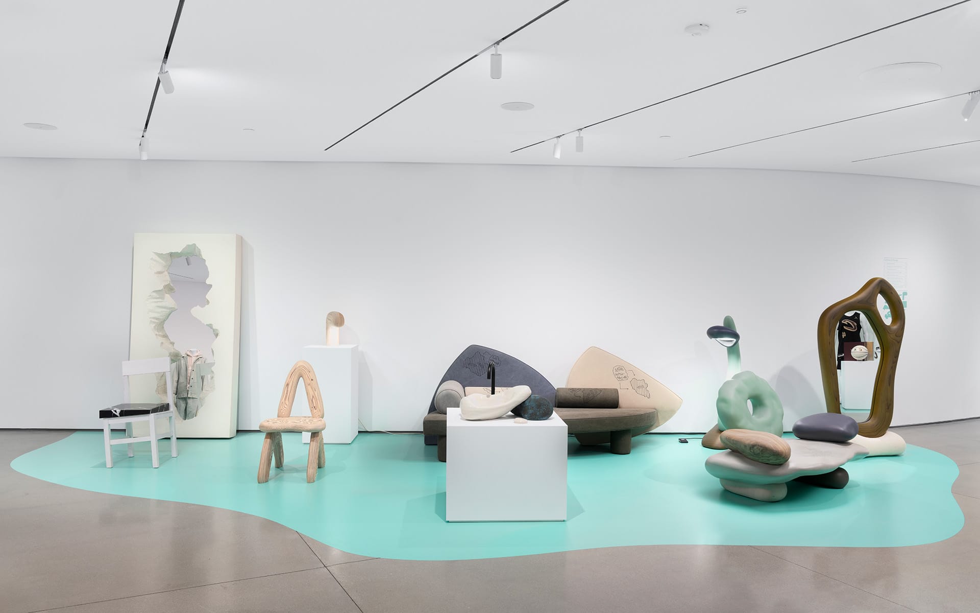 Contemporary art exhibit featuring various abstract sculptures and modern furniture displayed in a minimalist white gallery space.