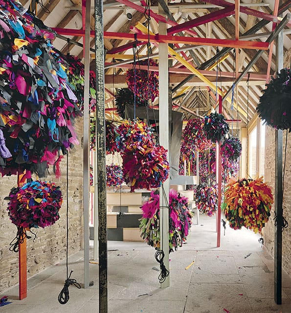 Colorful hanging art installations in a rustic room with wooden beams and stone walls.
