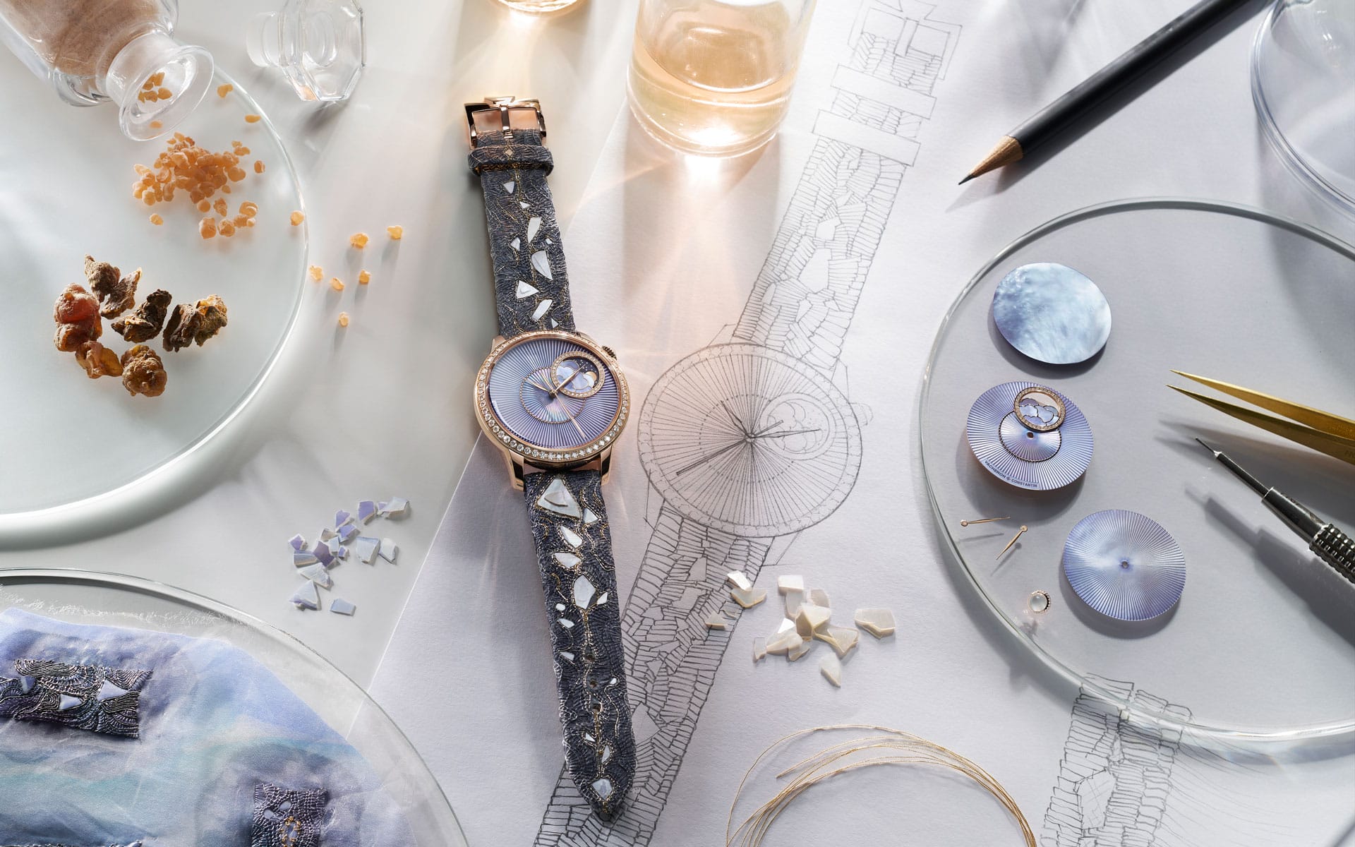 Elegant wristwatch with blue face on a table with watchmaking tools, blueprints, and decorative elements.