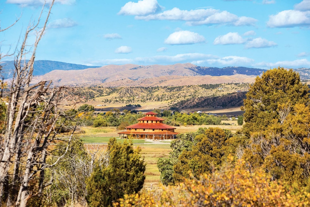 Scenic view of a large building surrounded by trees and rolling hills under a blue sky with scattered clouds.