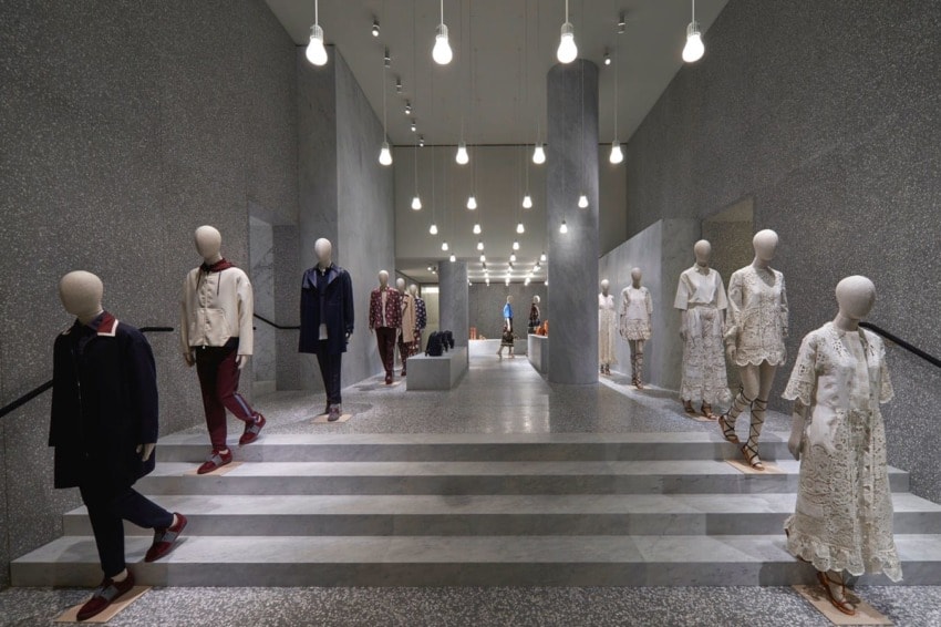 Mannequins wearing fashionable clothing displayed in a modern retail store interior with hanging lights.