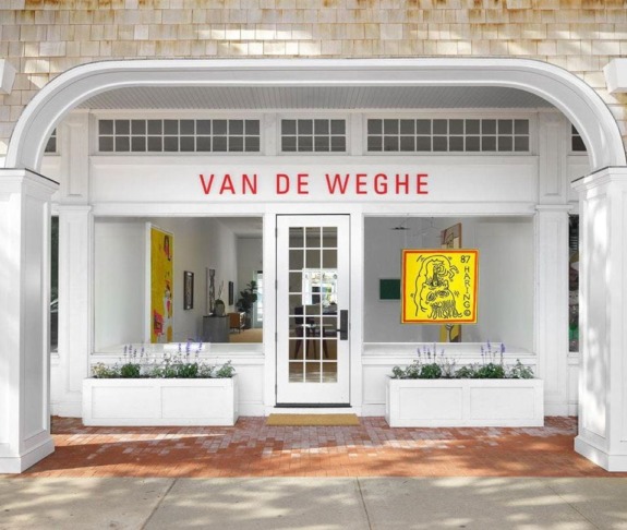 Front view of Van De Weghe art gallery with large windows, a glass door, and colorful artwork displayed inside.