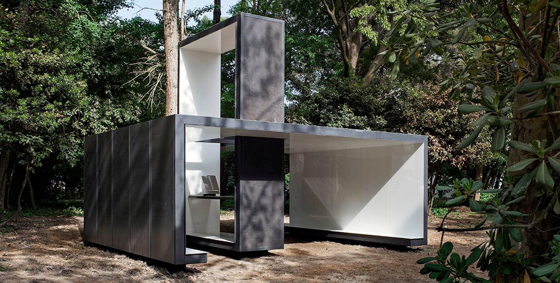 Modern minimalist modular building surrounded by lush green trees.