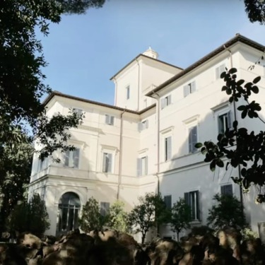 Historic white villa surrounded by trees and greenery against a clear blue sky.