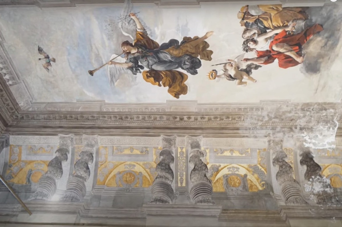 Ceiling fresco depicting an angel with a trumpet and figures in elaborate robes set against a classical architectural background.