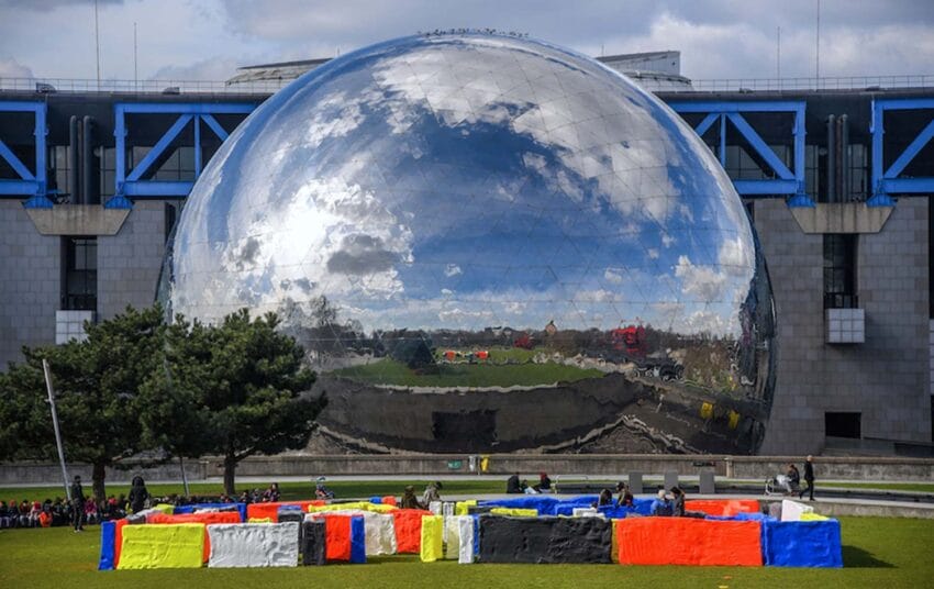 Reflective spherical building with colorful benches in front, set against a cloudy sky backdrop.