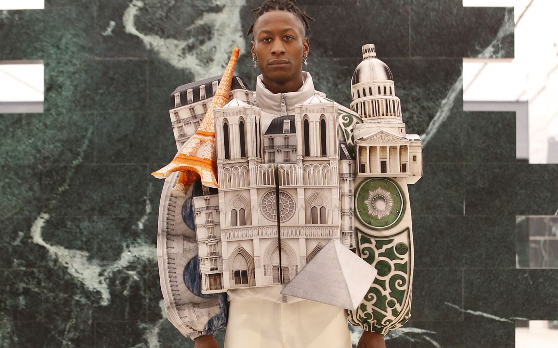 Model wearing an architectural-themed outfit with miniature buildings, including the Eiffel Tower and Notre-Dame Cathedral.