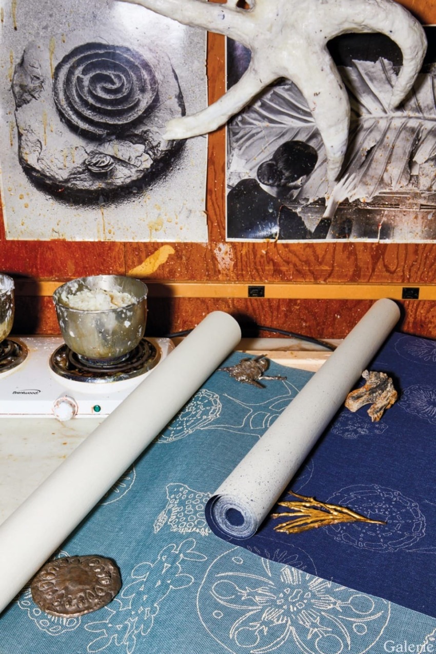 Art studio with sculpting materials, plaster casts, seashells, and textured fabric on a wooden table displaying creative chaos