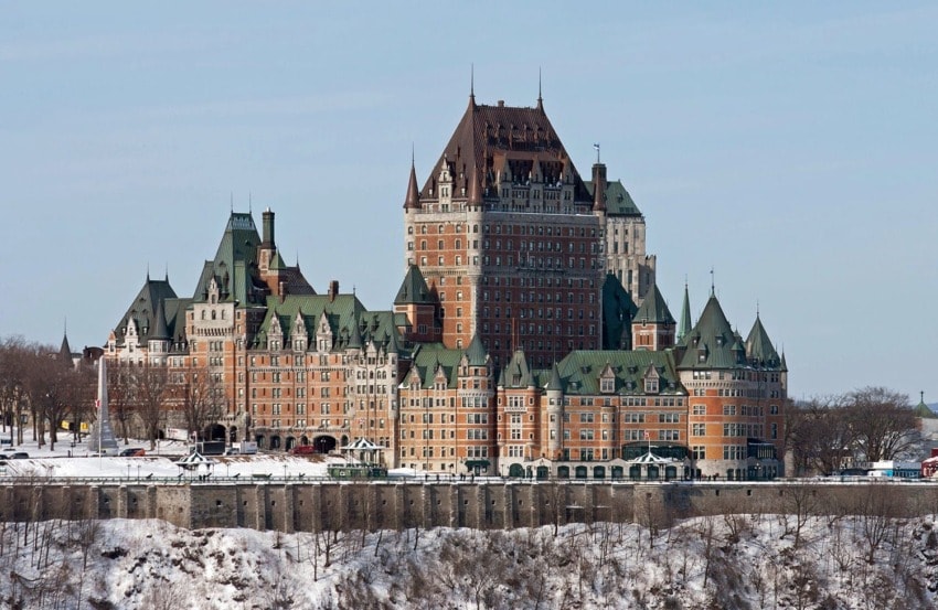Historic château with turrets and steep roofs on a snowy cliff, set against a clear blue sky.