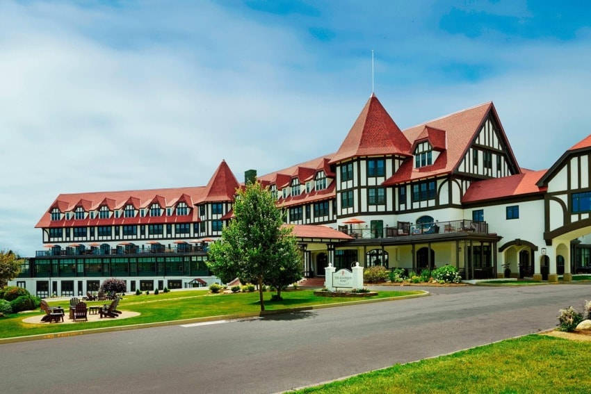 Large, historic hotel with red roof and Tudor-style architecture surrounded by green lawn and outdoor seating areas.