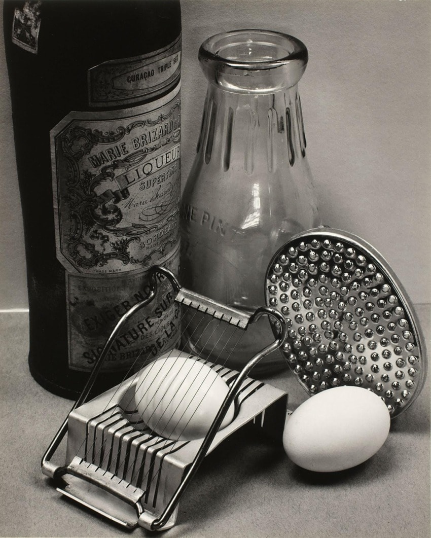 Vintage kitchen tools with eggs, glass bottle, and decorative liquor bottle on a countertop, creating a nostalgic scene.