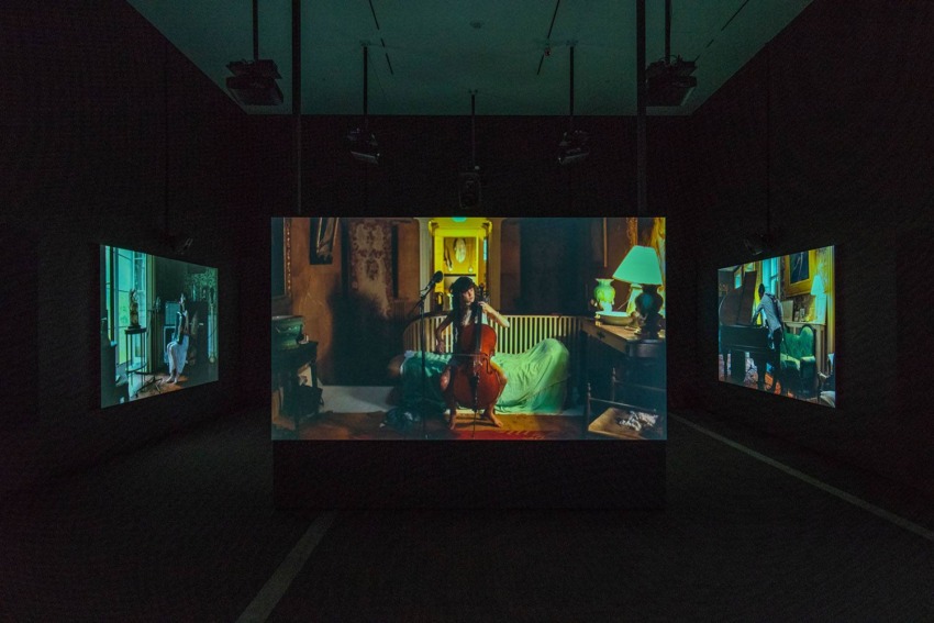 Three screens in a dark room showing a musician playing a cello, depicting a multi-angle immersive experience.