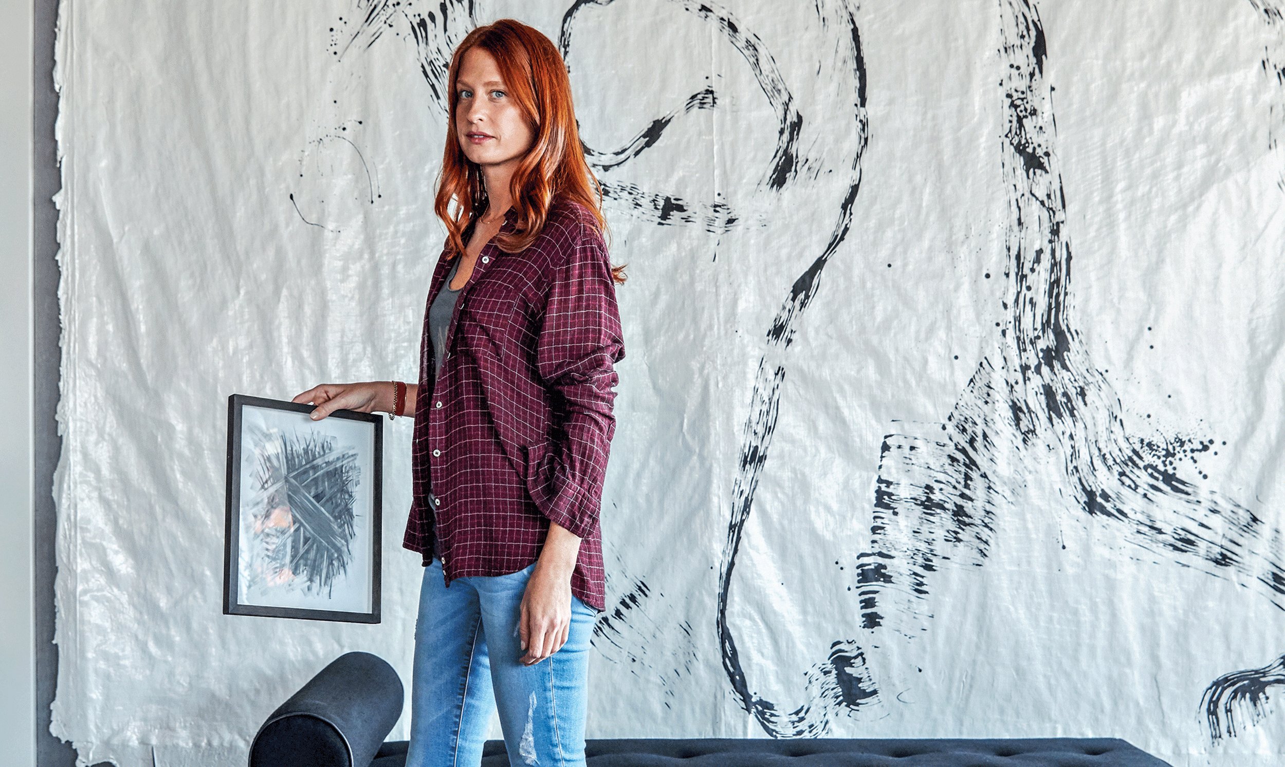 Person with a plaid shirt holding a framed picture, standing in front of abstract black and white wall art.