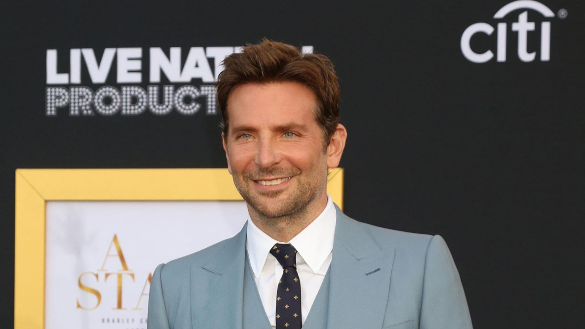 Man in a blue suit smiling at a film premiere event with a dark background.