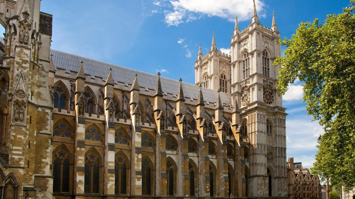 Exterior view of a historic Gothic cathedral with intricate architecture under a blue sky and surrounding greenery.