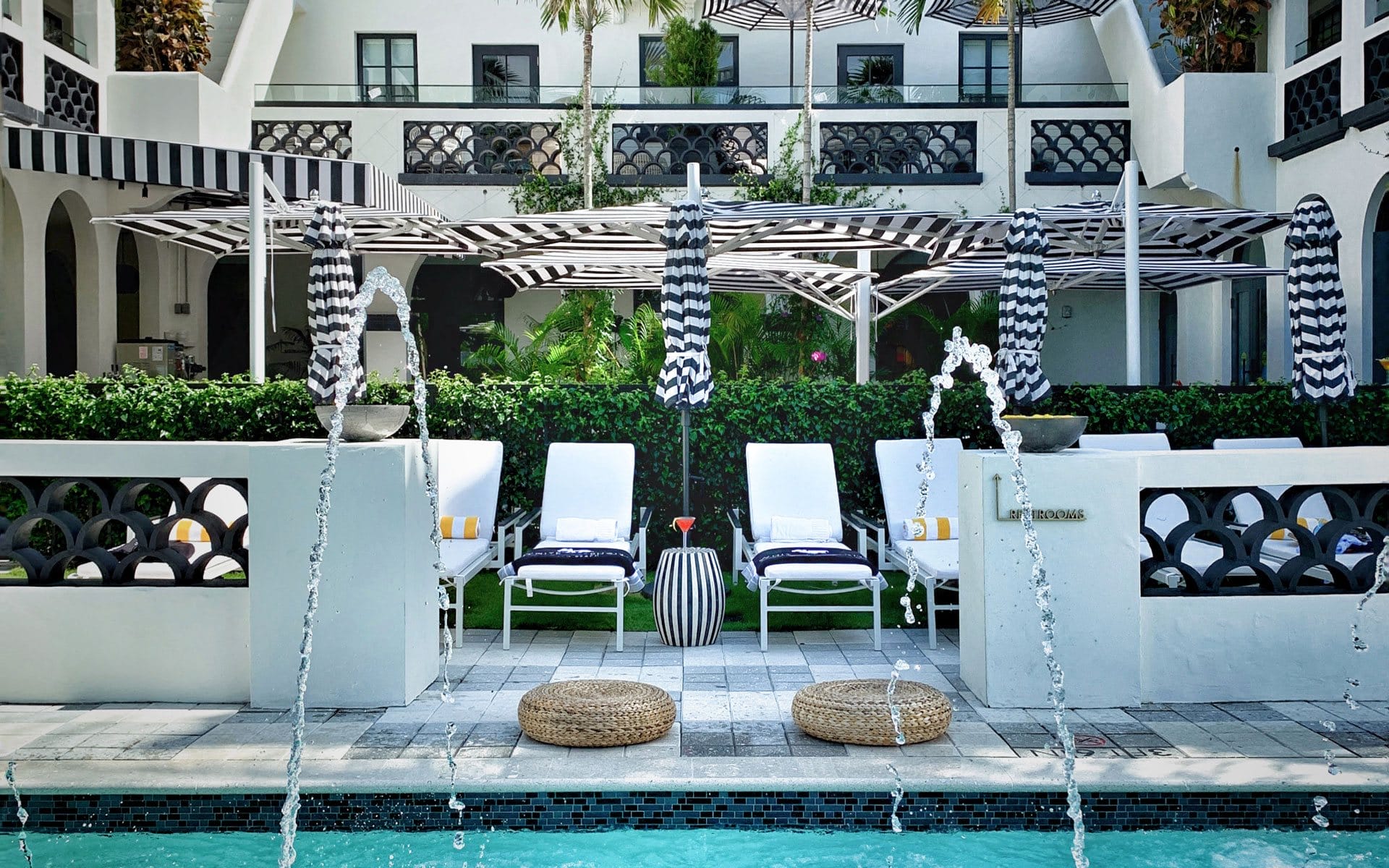 Luxurious poolside area with loungers, umbrellas, and decorative fountains against an elegant hotel backdrop.
