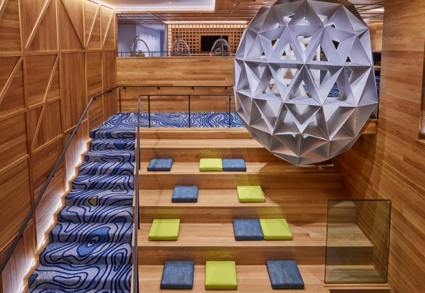 Modern staircase with geometric decor, patterned carpet, and colorful cushions on wooden steps in an artistic interior setting.