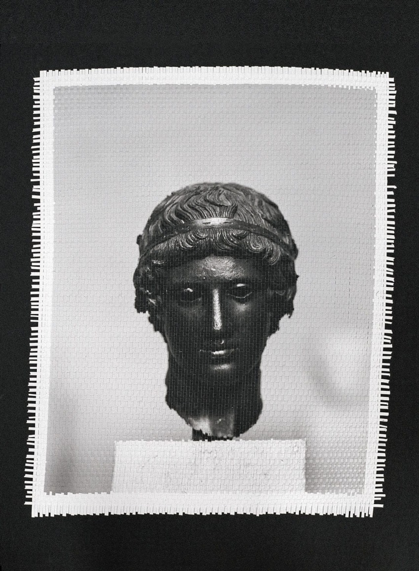 Black and white photo of an ancient statue head on a textured background with a dark frame.