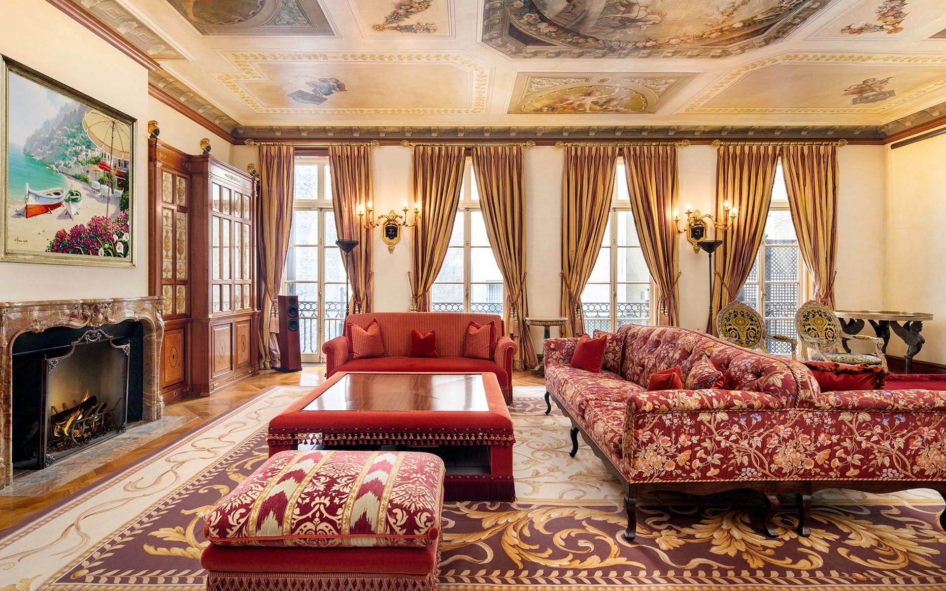Elegant living room with vintage furniture, ornate ceiling, patterned area rug, large windows, and a lit fireplace.