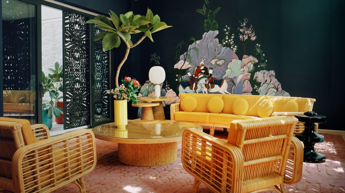 Stylish living room with wicker furniture, yellow sofa, and a nature-themed mural on a dark wall.