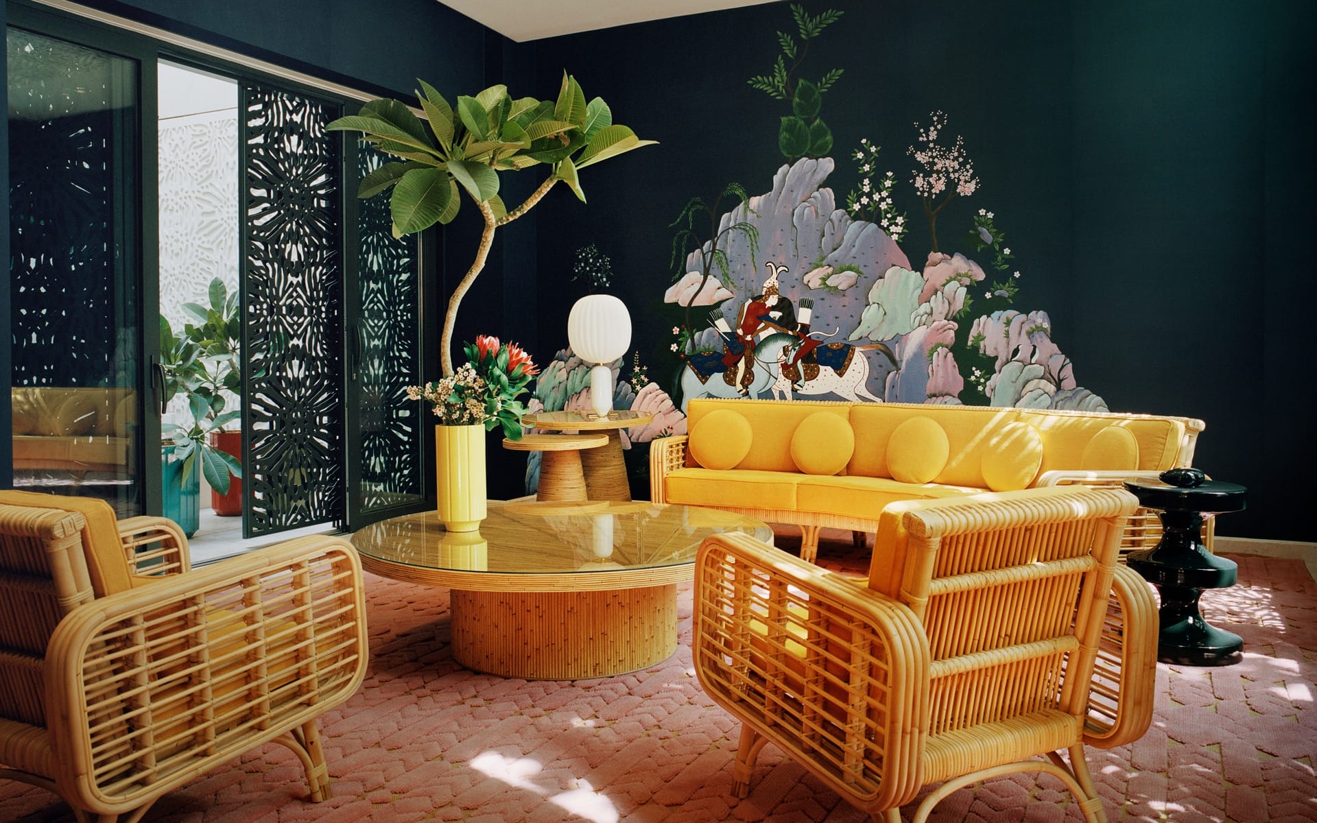 Stylish living room with wicker furniture, yellow sofa, and a nature-themed mural on a dark wall.