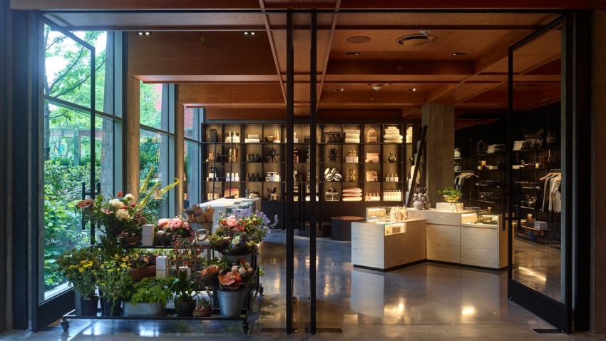 Modern shop interior with large windows, shelves of products, and vibrant floral display in the foreground.